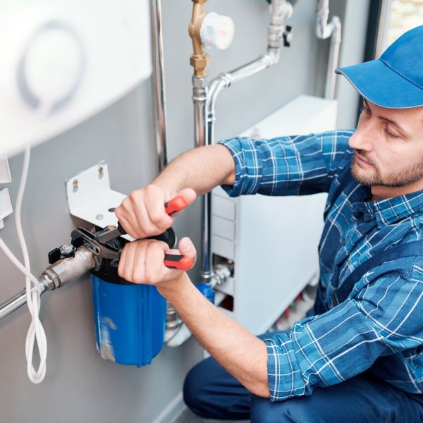 Young man in workwear using pliers while installing water filtration system
